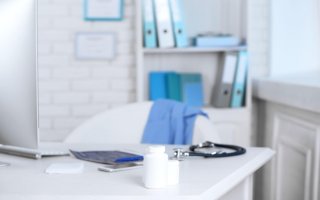 Bílá ambulance s fonendoskopem, léky, kalkulačkou a počítačem na stole.